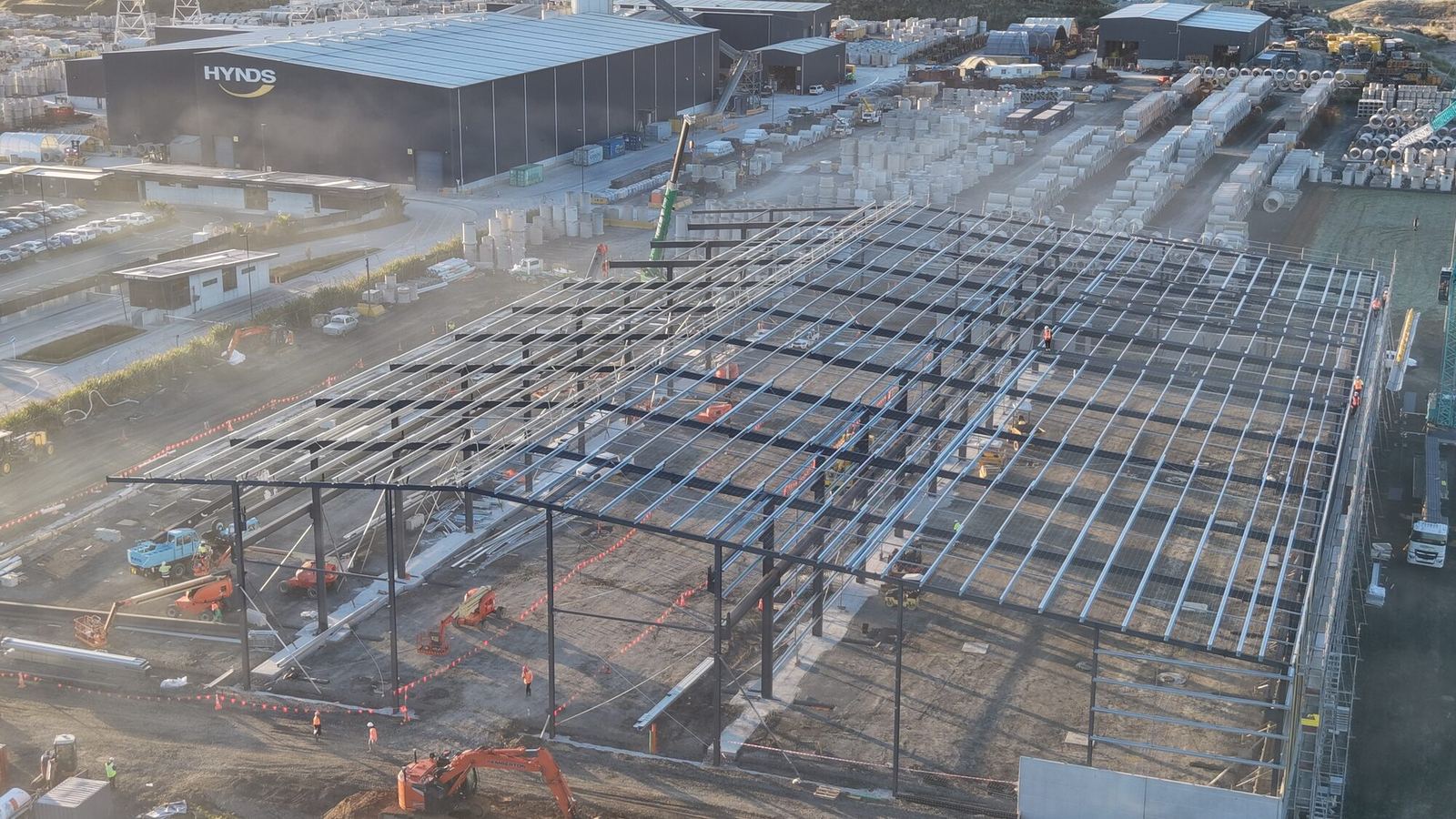 High aerial of the Hynds Pōkeno building with its full steel roof grid, beside the operating Hynds yard