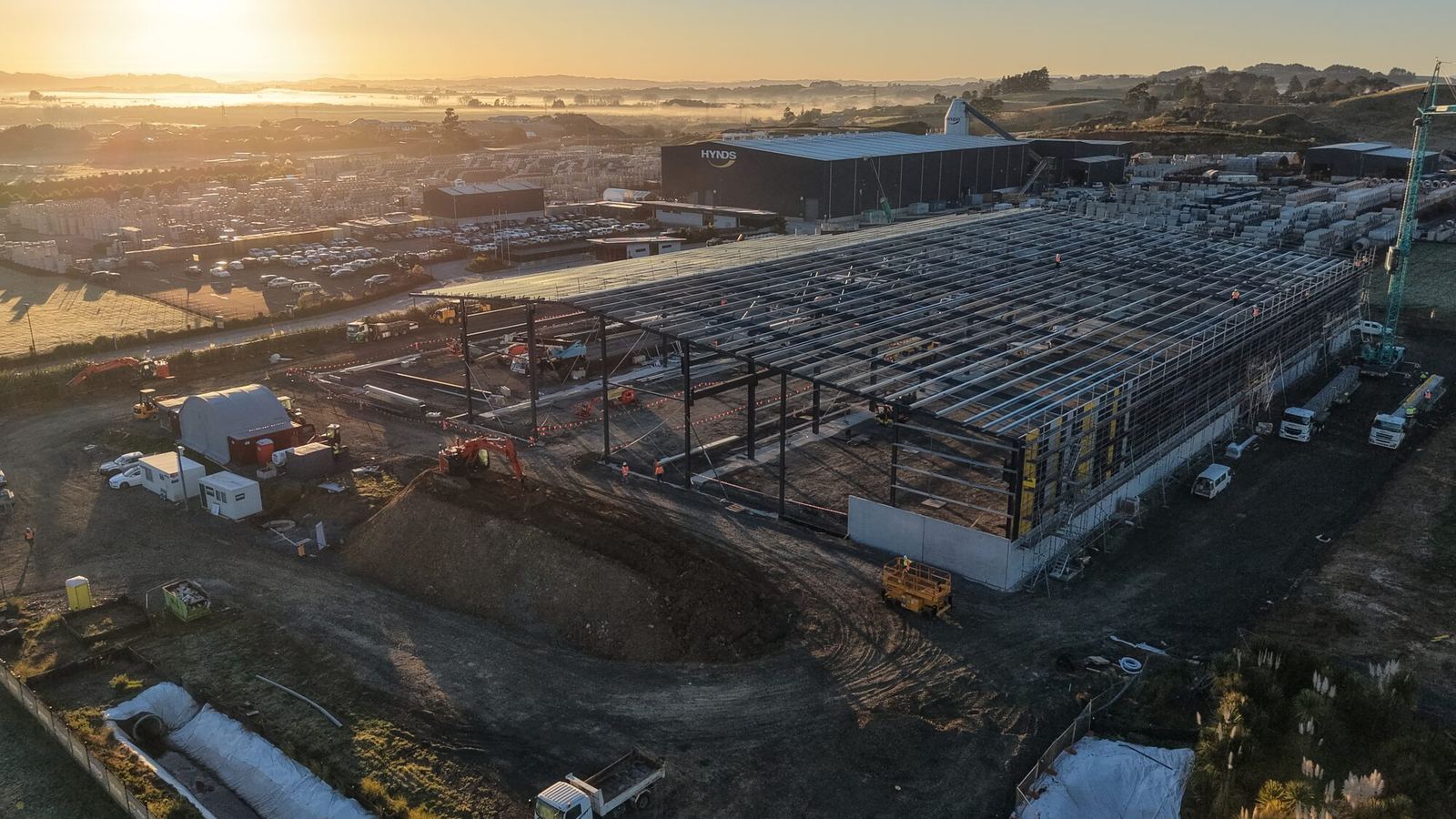 Sunrise aerial of the Hynds Pōkeno manufacturing facility under construction, steel portal frames and precast panels